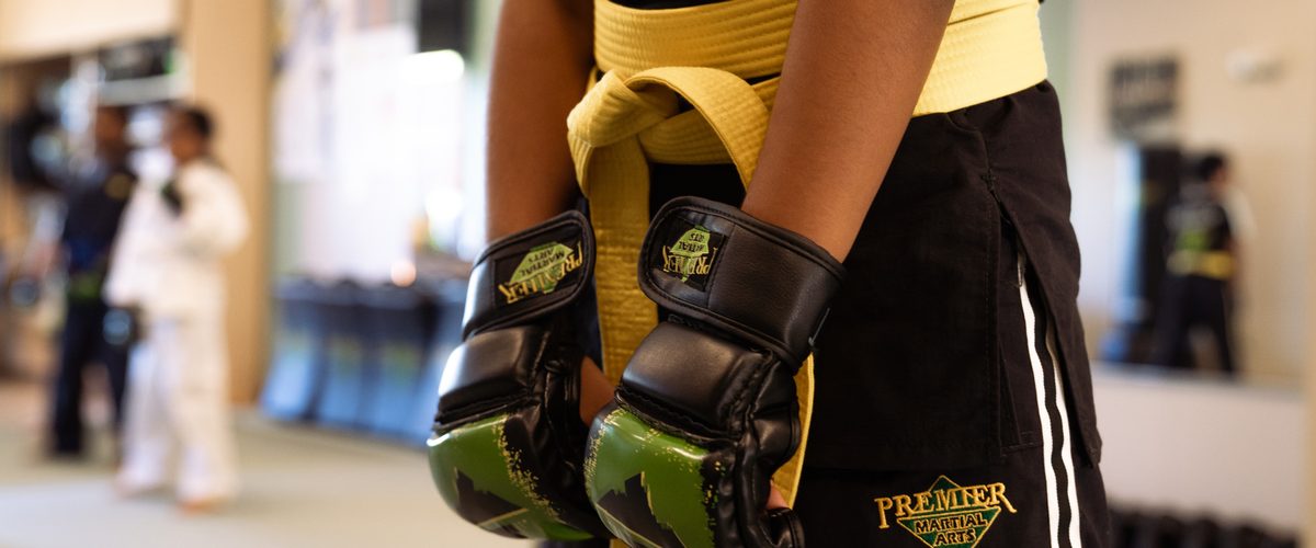 A young Premier Martial Arts student geared up with belt and gloves